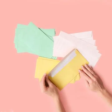 Colored paper envelopes hold human hands on a pink background. Top view. Pl.. Stock Photos