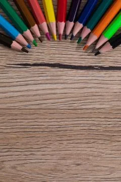 Colored pencil crayons arranged evenly on a wooden desk top. School supplies. Stock Photos