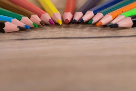 Colored pencil crayons arranged evenly on a wooden desk top. School supplies. Stock Photos