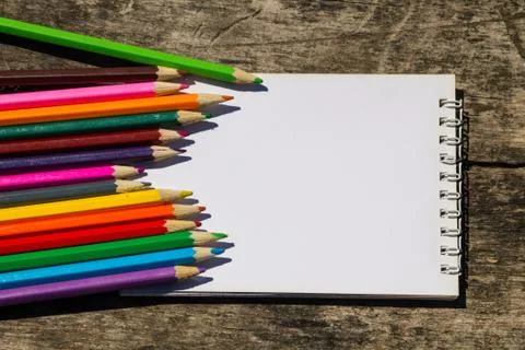 Colored pencils and blank notepad on old wooden desk Stock Photos