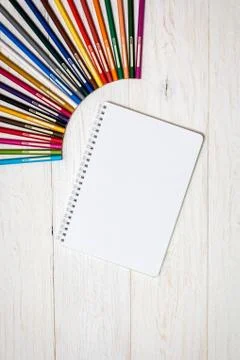Colored pencils and notepad on white boards Stock Photos