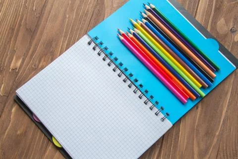 Colored pencils and opened notepad on wooden background Stock Photos
