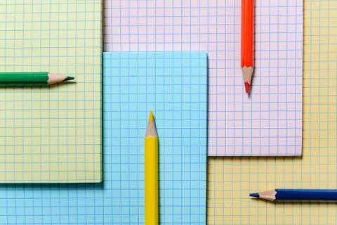 Colored pencils lie on the background of multi-colored notebook sheets. Stock Photos