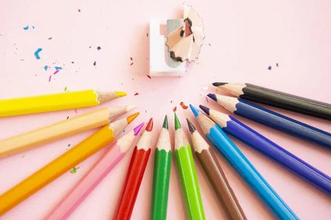 Colored pencils next to sharpener on light pink background Stock Photos