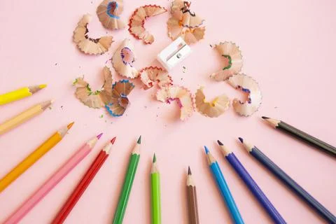 Colored pencils next to sharpener on light pink background Stock Photos