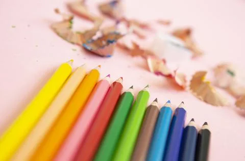 Colored pencils next to sharpener on light pink background Stock Photos