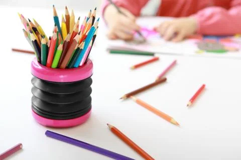 Colored pencils on the table and drawing the child in the backround  Stock Photos