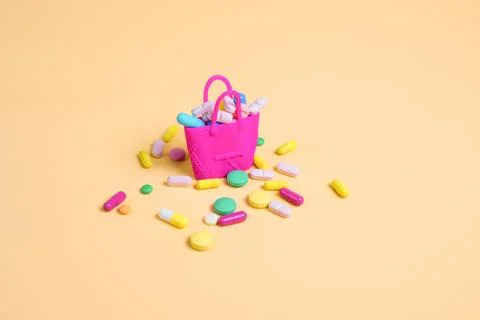 Colored pills fall out of a pink handbag on an orange background Stock Photos