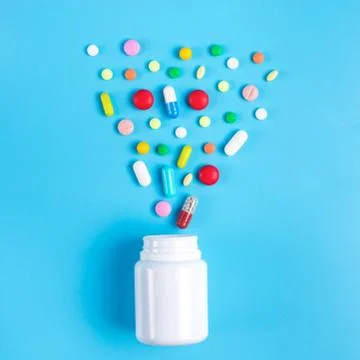 Colored pills, tablets and white bottle on blue background Stock Photos