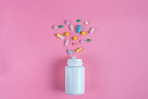 Colored pills, tablets and white bottle on pink background Stock Photos