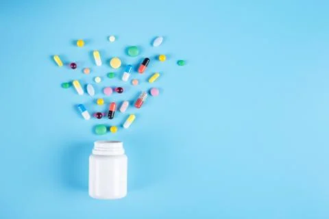 Colored pills, tablets and white bottle on blue background Stock Photos