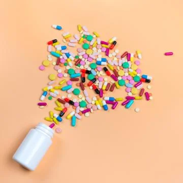 Colored pills, tablets and white bottle on orenge background Stock Photos