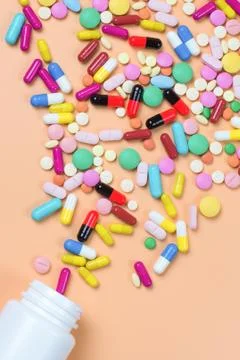 Colored pills, tablets and white bottle on orenge background Stock Photos