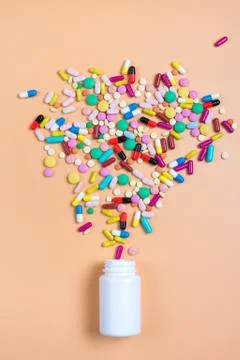 Colored pills, tablets and white bottle on orenge background Stock Photos