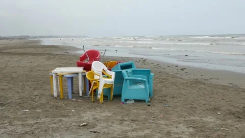 Colored plastic chairs and tables stacked on a deserted, windswept beach Stock Footage 317966089