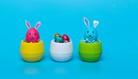 In colored pots Easter eggs with hare ears stand on a blue background Stock Photos