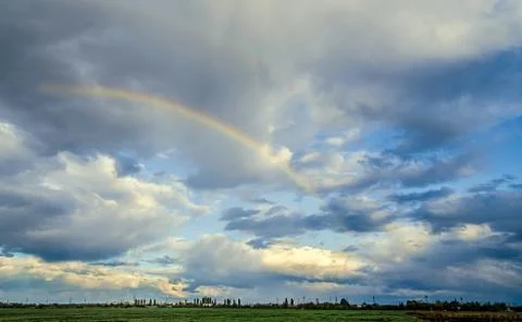 Colored rainbow over blue sky, rainy day. Stock Photos