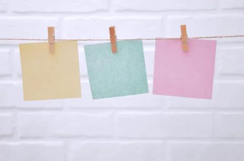 Colored sheets of paper are hung on the rope with clothespins on a white back Stock Photos