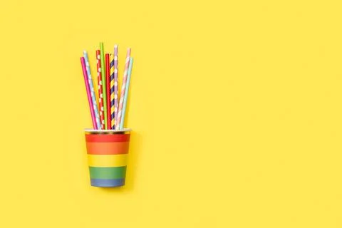 Colored striped drinking straws in a colored disposable glass on a yellow bac Foto stock