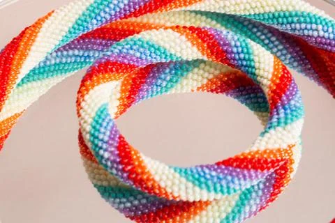 Colored weaving of a beaded bracelet. Reflection on a glass table. Close up. Stock Photos