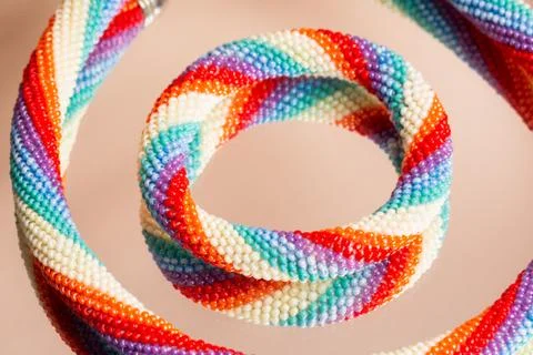 Colored weaving of a beaded bracelet. Reflection on a glass table. Close up. Stock Photos