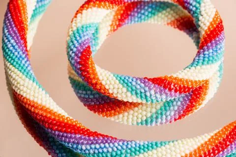 Colored weaving of a beaded bracelet. Reflection on a glass table. Close up. Stock Photos