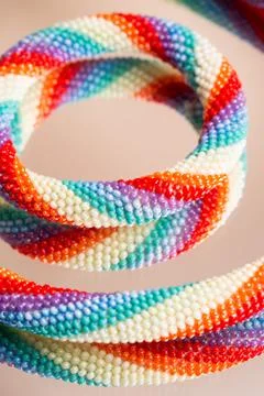 Colored weaving of a beaded bracelet. Reflection on a glass table. Close up. Stock Photos