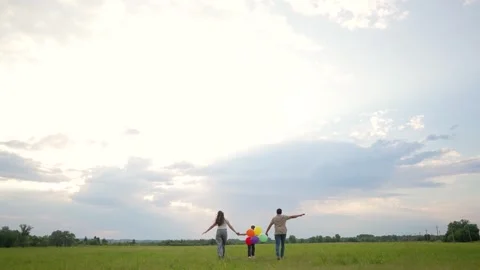 Colorful balloons float above grassy field while child walks with parents at Stock Footage 345958446