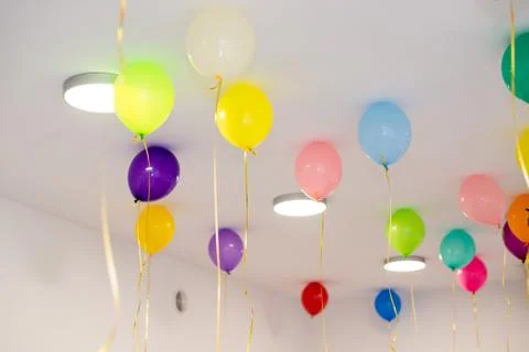 Colorful balloons hang under the white ceiling. Stock Photos