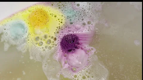 Colorful bath bombs spin and fizz in bathtub water Stock Footage 334053506