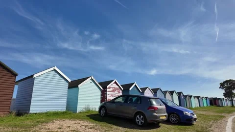 Colorful beach huts lined up under a bright blue sky with wispy clouds Stock Footage 337873172
