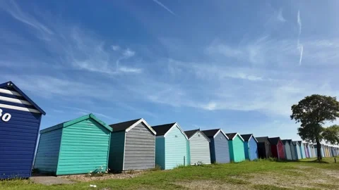 Colorful beach huts lined up under a bright blue sky with wispy clouds Stock Footage 337873265