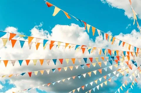Colorful bright triangular Bunting flags on a blue sky background with white 写真素材