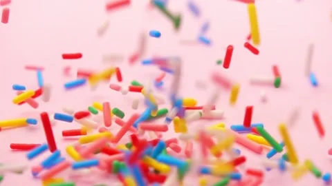 Colorful cascade of sprinkles flows in slow motion, set against serene pink.. Stock Footage 330986996