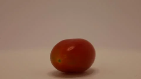 Colorful cherry tomato rolling playfully on a smooth surface in an indoor settin Stock Footage 328633144