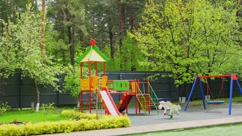 Colorful children's playground stands empty against a lush green forest Stock Footage 335580068