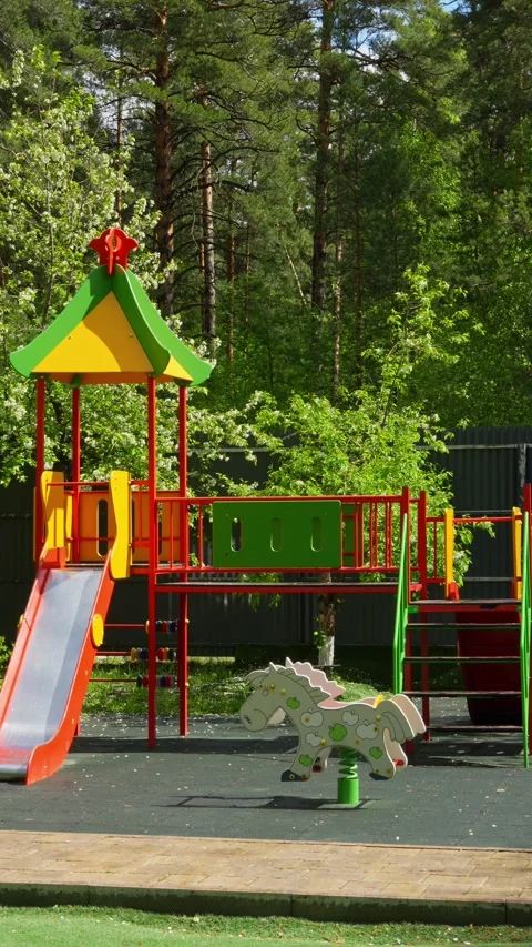 Colorful children's playground stands empty against a lush green forest Stock Footage 335580363