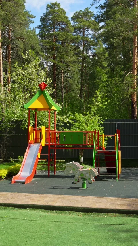 Colorful children's playground stands empty against a lush green forest Stock Footage 335580523