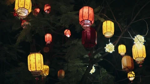 Colorful Chinese lanterns dangling from tree branches, swirling softly under Stock Footage 315525785
