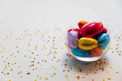 Colorful chocolate easter eggs in a transparent bowl with white background an Stock Photos