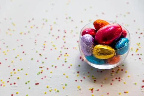 Colorful chocolate easter eggs in a transparent bowl with white background an Stock Photos