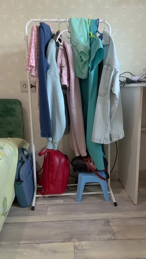 Colorful clothes hanging on a white rack in a bedroom with red backpack Stock Footage 341702576