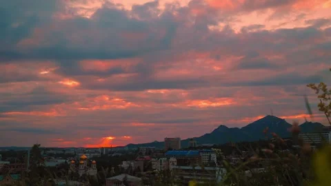 Colorful clouds fill the sky as the sun sets behind the mountains, casting a Video stock 312148024