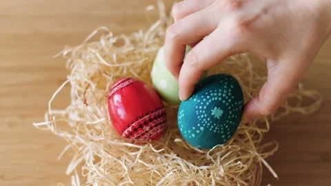 Colorful decorated Easter eggs being placed in a hay nest on wooden background. Stock Footage 149062744