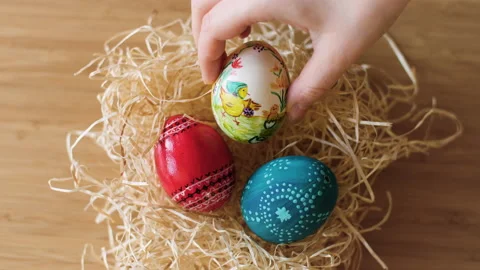 Colorful decorated Easter eggs being placed in a hay nest on wooden background. Stock Footage 149063307