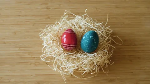 Colorful decorated Easter eggs being placed in a hay nest on wooden background. Stock Footage 149064831