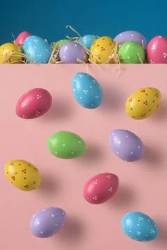 Colorful dotted Easter eggs drop from above onto pastel pink background, with Stock Photos