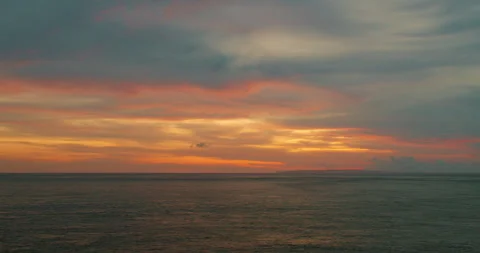 Colorful dramatic sunset over ocean horizon with dark clouds and smooth tranquil Stock Footage 326016423