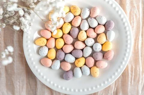 Colorful Easter chocolate eggs in a plate with flowers on a beige background Stock Photos