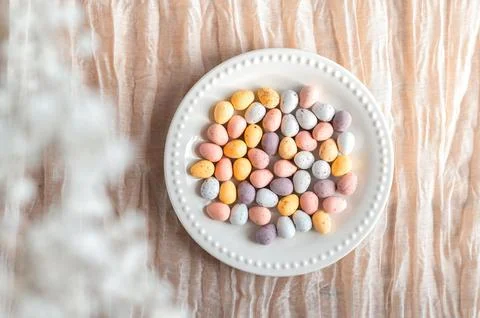 Colorful Easter chocolate eggs in a plate with flowers on a beige background Stock Photos